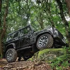 A black SUV with Cooper Discoverer all-terrain tires climbing over a rock on a forest trail.
