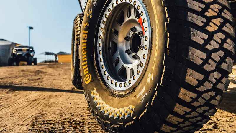 A close-up of a rugged Continental all-terrain tire on a truck in the dirt.
