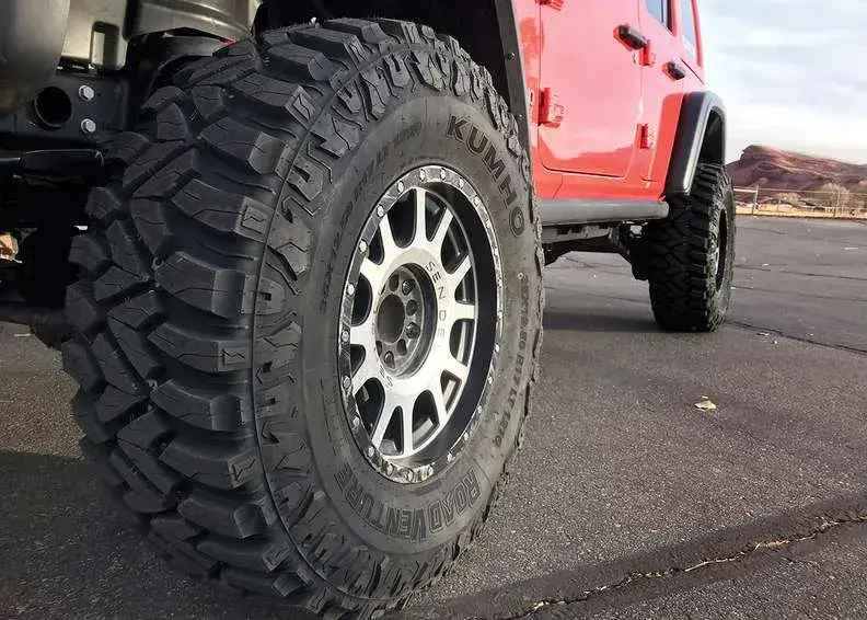 A close-up of a Kumho Road Venture mud-terrain tire on a red Jeep.
