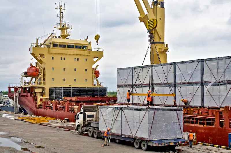 A crane loading cargo from a ship onto a truck, representing the global logistics industry supported by Americus commercial tires. 