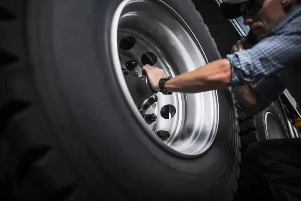 A technician performing maintenance on a heavy-duty Cosmo commercial truck wheel.